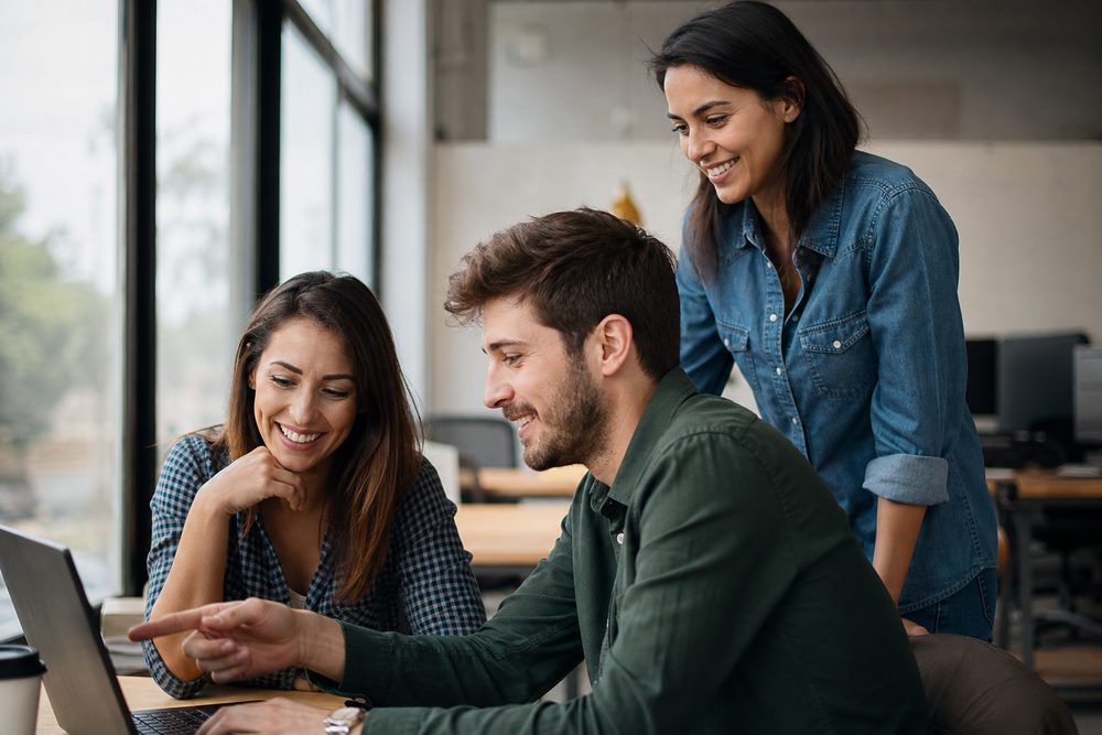 A small team collaborating around a laptop in a bright office—an example of the lean teams Knockout Networks supports.