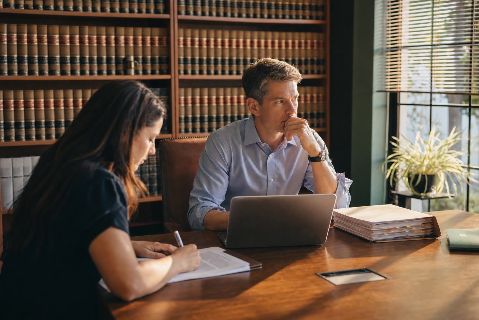 Attorney and paralegal working with documents and a laptop at a conference table in a small law firm library.
